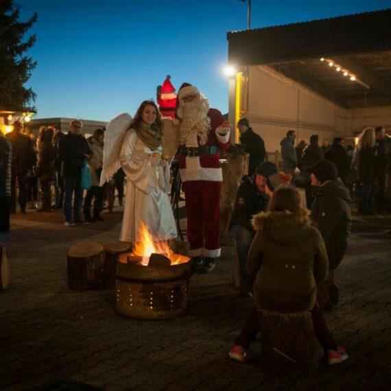 Schumacher Weihnachtsmarkt mit einem Engel und dem Weihnachtsmann die vor einer großen Feuerschale stehen